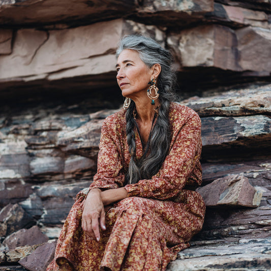 Contemplative elder woman with braided gray hair reflecting on ancestral wisdom amid rocky landscape, embodying inner peace and cultural roots